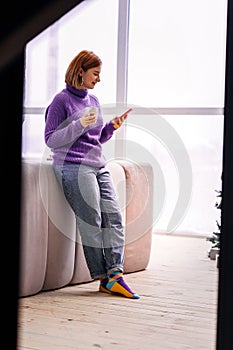 Young cute beaming girl in bright socks standing near the window