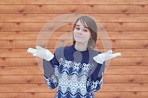 Young cute beautiful girl in a sweater on the background of a boardwalk shrugs