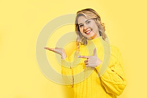 Young cute beautiful smiling woman wearing yellow sweater standing over yellow background, pointing with hand and finger to copy photo