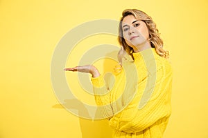 Young cute beautiful woman wearing yellow sweater standing over yellow isolated background, smile on face, pointing with hand to photo
