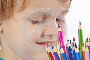 Young cute blond boy looks on color pencils