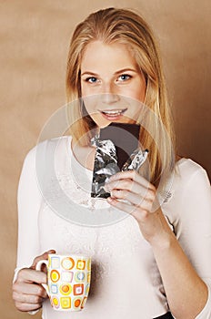 Young cute blond girl eating chocolate and drinking coffee close up