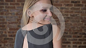 Young cute blond girl is winking, flirt concept, brick background