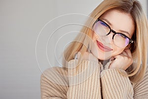 Young cute blonde with eyeglasses and a beige sweater. Stylish fashionable young woman.