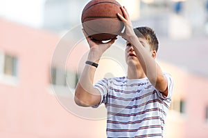 A young cute boy plays basketball at the outdoor streetball court on a sunny summer day. Teenager player in action with the ball.