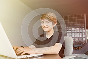 Young cute boy using laptop computer while sitting at the table in living room at home. Look at camera.