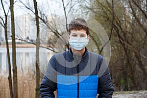 Young cute caucasian boy wearing protective mask against the corona virus on the street. Teenager in surgical  face mask