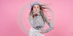 Young cute caucasian lady with flying hair in a fashionable beret on a pink background