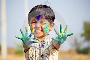 Young cute cheerful little girl kid with applied holi colors powder showing colorful hands to camera during holi festival