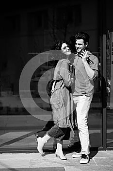 Young cute couple - a boy and a girl standing near a glass building. The couple spend time together. The guy speaks on the phone,