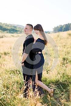 Young cute couple in love, wearing stylish black clothes, posing outdoor in summer meadow. Sensual romantic portrait of