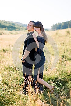 Young cute couple in love, wearing stylish black clothes, posing outdoor in summer meadow. Sensual romantic portrait of