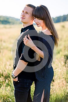 Young cute couple in love, wearing stylish black clothes, posing outdoor in summer meadow. Sensual romantic portrait of