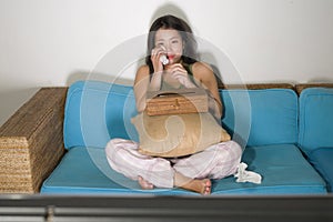 Young cute and emotional Asian Chinese woman watching korean drama show on TV sitting at home living room couch crying wiping