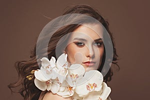 Young cute female face with healthy brown hair, clear skin, natural makeup and white orchid flowers portrait