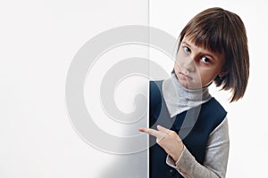 Young cute girl behind white empty banner. She pointing to white wall. Free copyspace area