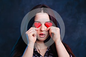 Young cute girl covering eyes with fabric hearts, studio shoot.