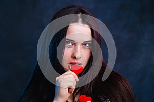 Young cute girl holding in hands and biting fabric hearts, studi