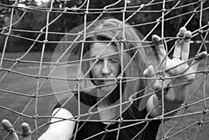 Young cute girl looking through the net of football goal. Black and white photo.
