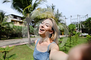 Young cute girl making video call by smartphone near palm trees in background.