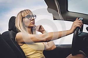 Young cute girl preens while driving. blonde admires herself in mirror.