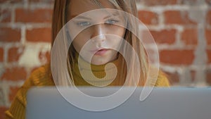 Young cute girl is sitting near the laptop and looking at the screen. Concept of gadget use.