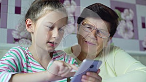 Young cute granddaughter teaching grandmother how to use smartphone at home