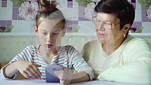 Young cute granddaughter teaching grandmother how to use smartphone at home