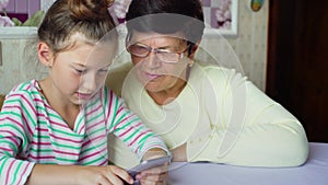 Young cute granddaughter teaching grandmother how to use smartphone at home