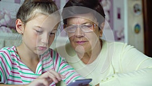 Young cute granddaughter teaching grandmother how to use smartphone at home