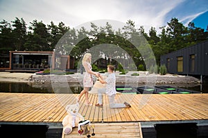 Young cute guy makes a marriage proposal to his beloved girl, standing on his knee on a wooden pier. Romance and love on a wooden