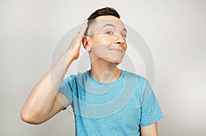 Young cute guy pretend comic macho with a smirk, dressed in a blue t shirt on a light background