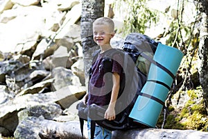 Young cute happy child boy with big tourist backpack on sunny rocks background. Tourism, hiking and active lifestyle concept