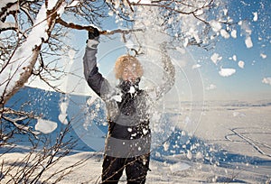 Young cute happy laughing female woman model playing with snowy trees branches smiling from fun and joy in falling down white snow