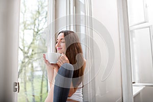 Young and cute lady dreaming on the windowsill with cup of coffee