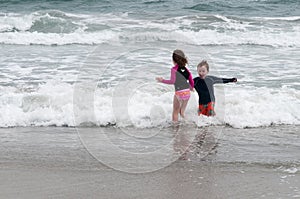 Young cute little boy and girl playing at the seaside running into the surf on a sandy beach in summer sunshine