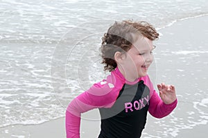 Young cute little girl playing at the seaside running into the surf on a sandy beach in summer sunshine