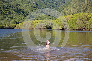 Young cute little girl playing in the water in a beautiful river on a sunny summer day