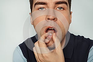 Young cute man sucks a pill from inflammation of the tonsils. . man eating pills cough sore throat pastille colorful. a mint for