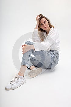Young cute pensive caucasian girl posing in white shirt, blue jeans at studio