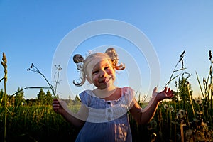 Young cute pretty funny girl in a meadow with dandelion flowers in the light of the sun at sunset and blue sky background. Girl