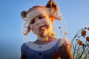 Young cute pretty funny girl in a meadow with dandelion flowers in the light of the sun at sunset and blue sky background. Girl