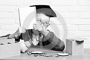 Young cute pupil boy in grey sweater and glasses sitting at desk with copybook in hand wooden numbers pink piggy pig