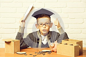 Young cute pupil boy in grey sweater and glasses sitting at desk with copybook in hand wooden numbers pink piggy pig