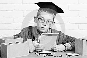 Young cute pupil boy in grey sweater and glasses sitting at desk with copybook in hand wooden numbers pink piggy pig