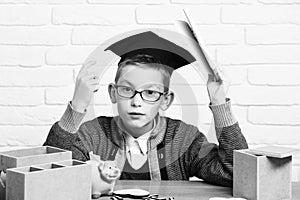 Young cute pupil boy in grey sweater and glasses sitting at desk with copybook in hand wooden numbers pink piggy pig