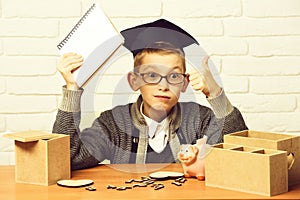 Young cute pupil boy in grey sweater and glasses sitting at desk with copybook in hand wooden numbers pink piggy pig