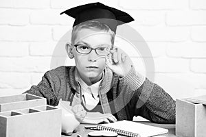 Young cute pupil boy in grey sweater and glasses sitting at desk with copybook wooden numbers pink piggy pig bank in