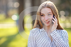 Young cute smiling woman talking on smart phone outdoors. Conver