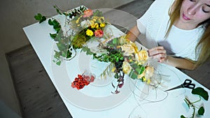 Young cute woman designer colors creates from flowers custom made thematic compositions, at table in office by day.n